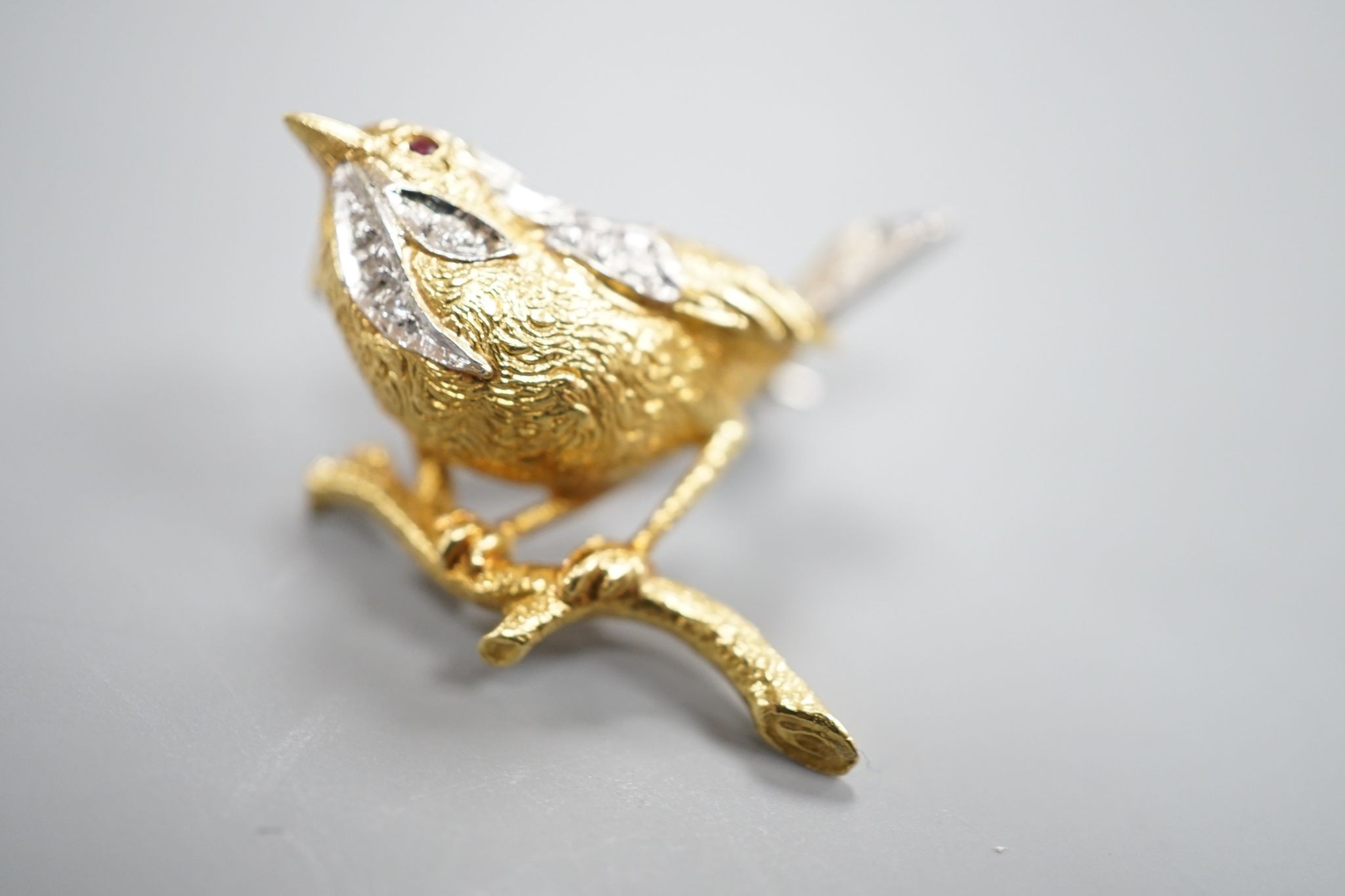 A modern textured 18ct two colour gold, ruby and diamond set bird brooch, 24mm, gross weight 6 grams.